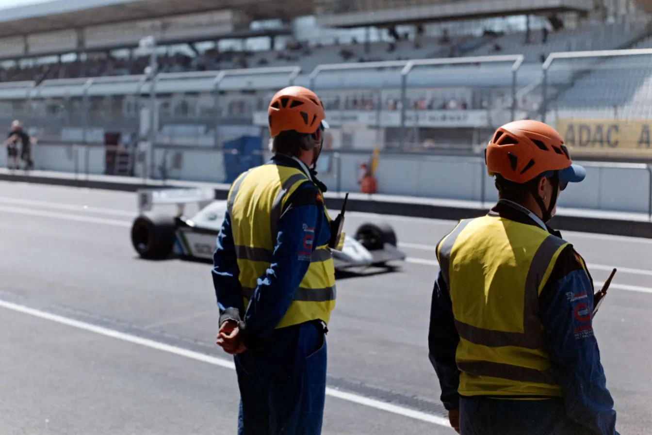 Deux commissaires en gilet jaune et casque orange surveillent piste, symbole des missions pour devenir commissaire de course automobile.