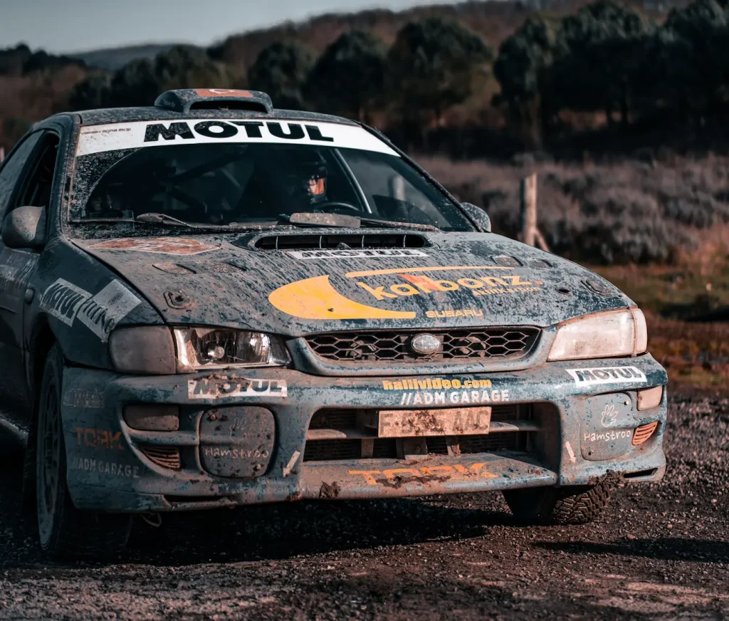 Subaru bleue couverte de boue garée sur piste, symbole des courses de rallye comparées aux circuits courts et intenses du rallycross.