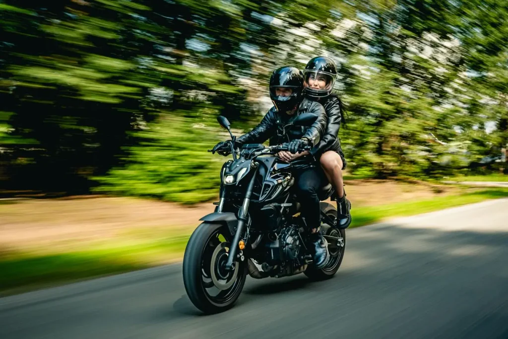 Deux personnes circulent à moto sur une route bordée d’arbres, illustrant les différentes catégories de conduite concernées par l’équivalence des permis moto