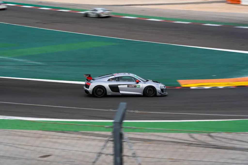 Voiture de course argentée et noire filant sur circuit, symbole des besoins spécifiques d’une assurance adaptée aux compétitions automobiles.