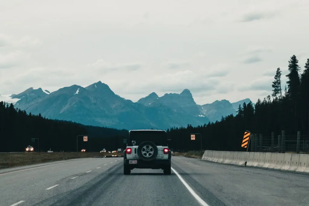Voiture roulant sur autoroute bordée de sapins et montagnes enneigées, symbole des trajets surveillés par radar tronçon.