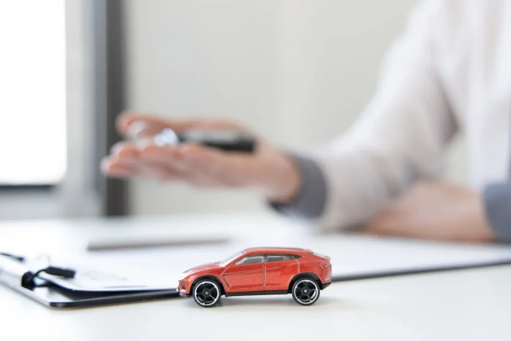 Petite voiture rouge posée sur bureau blanc près d’un stylo et documents, symbole de l’assurance auto pour véhicule de collection.