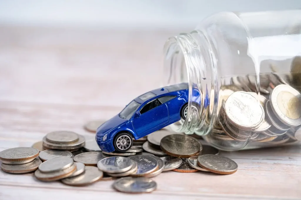Petite voiture bleue sortant d’un bocal rempli de pièces, symbole des économies liées à l’assurance jeune conducteur avec boîte noire.