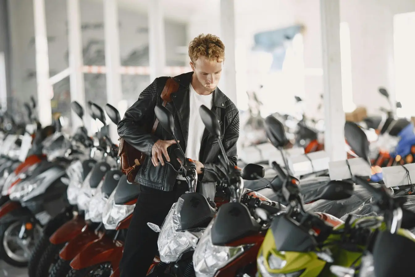 choisir une première moto Personne découvrant plusieurs motos exposées dans une concession, comparant les modèles pour choisir une première moto 125 cm3 adaptée à ses besoins