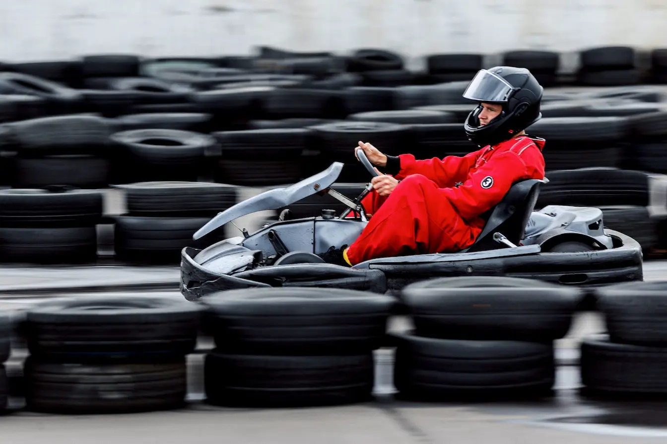 karting Pilote en combinaison rouge et casque noir conduisant kart sur piste entourée de pneus, symbole des règles de sécurité imposées par la licence FFSA.