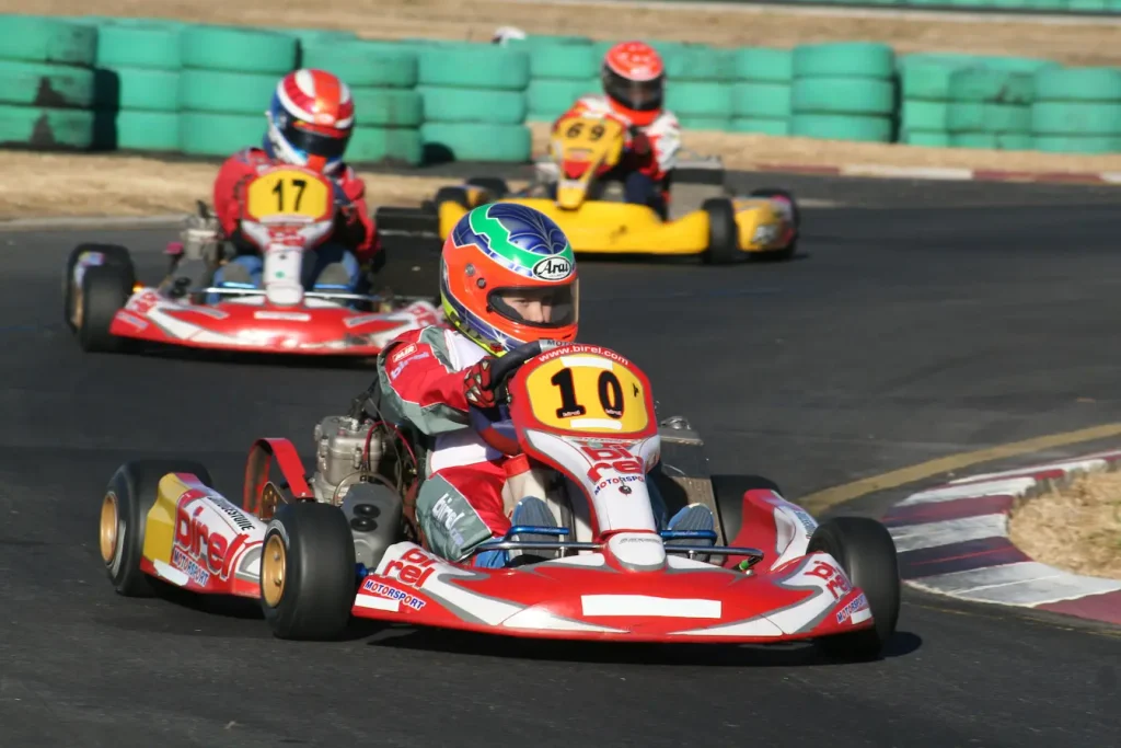 Trois pilotes en kart sur piste avec combinaisons et casques, symbole des règles de sécurité imposées par la licence FFSA.