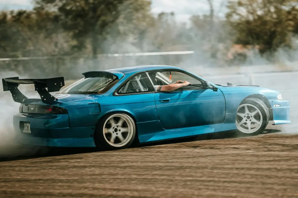 Une voiture de course bleue effectue une violente dérive sur piste en dégageant beaucoup de fumée blanche par ses pneus.